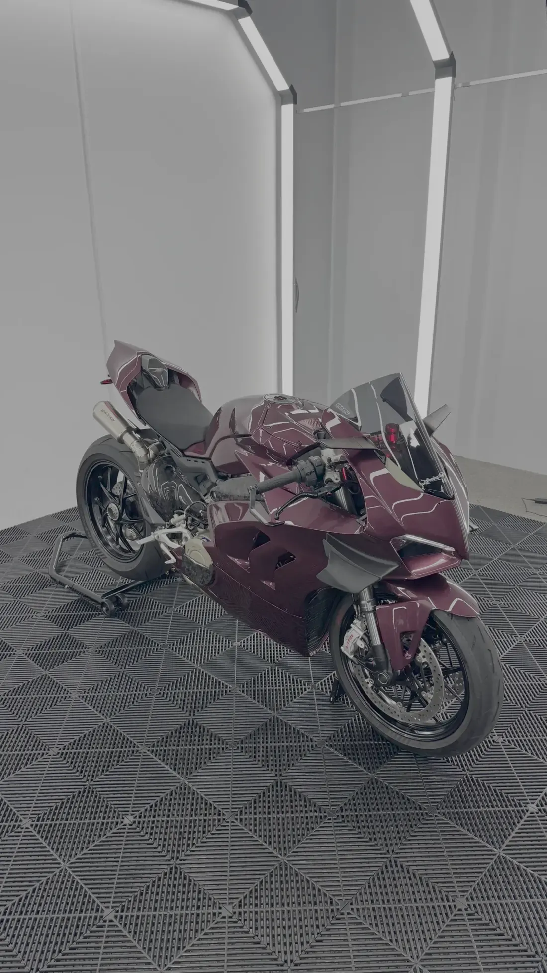 A superbike in a deep burgundy wrap with white flow-line graphics, on a stand in a white workshop.